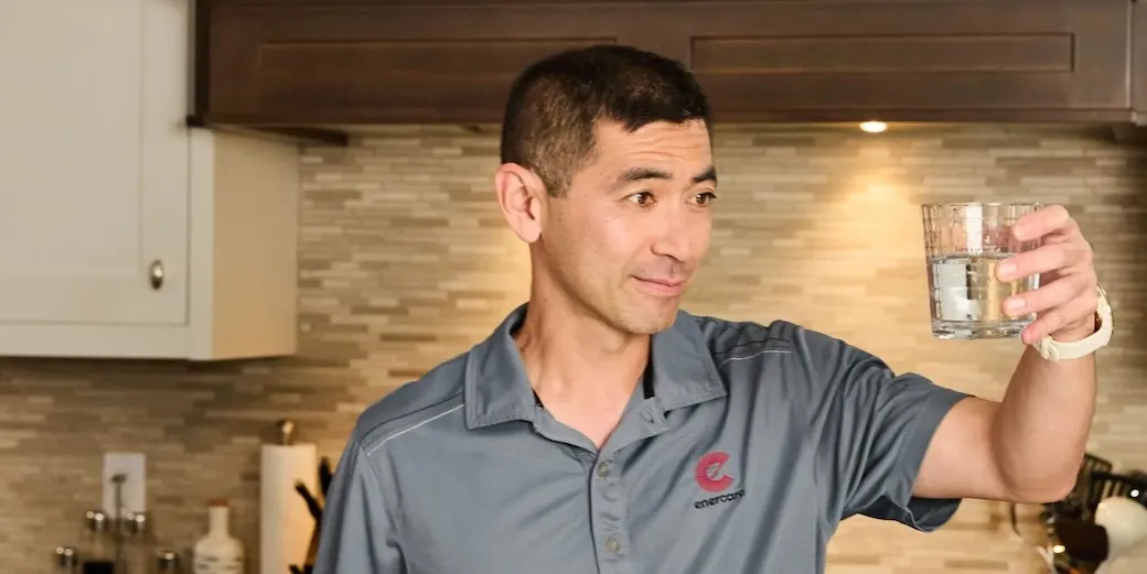 Man in an Enercare shirt holding up a glass of water and looking at it